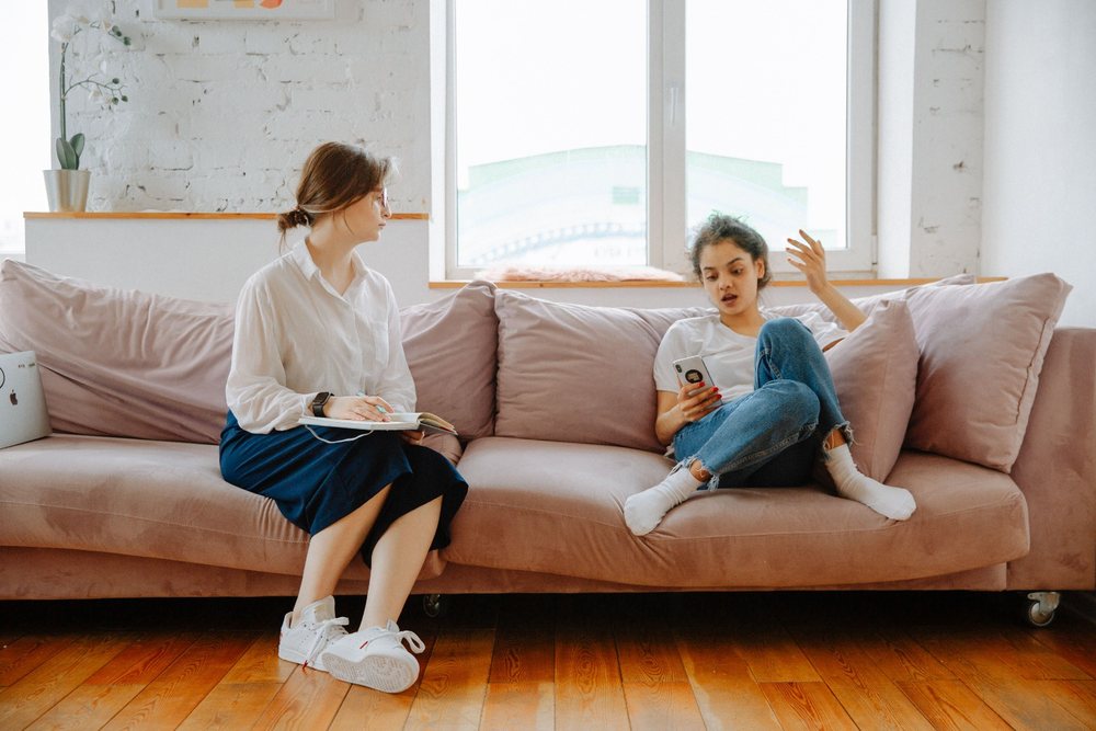 A key worker sitting with a teenage girl on a sofa, notebook in hand, talking things through.