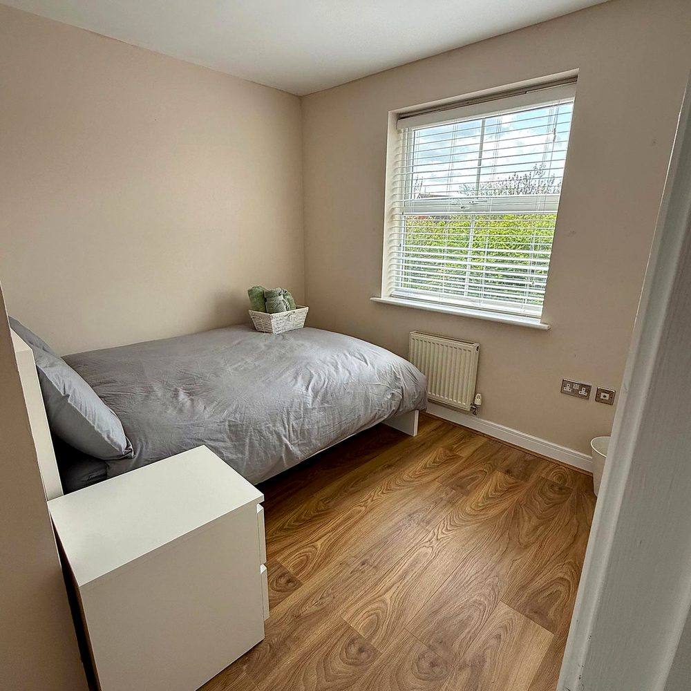 A bedroom at Hammond House with a bed, desk, chair and storage, and daylight from the window.